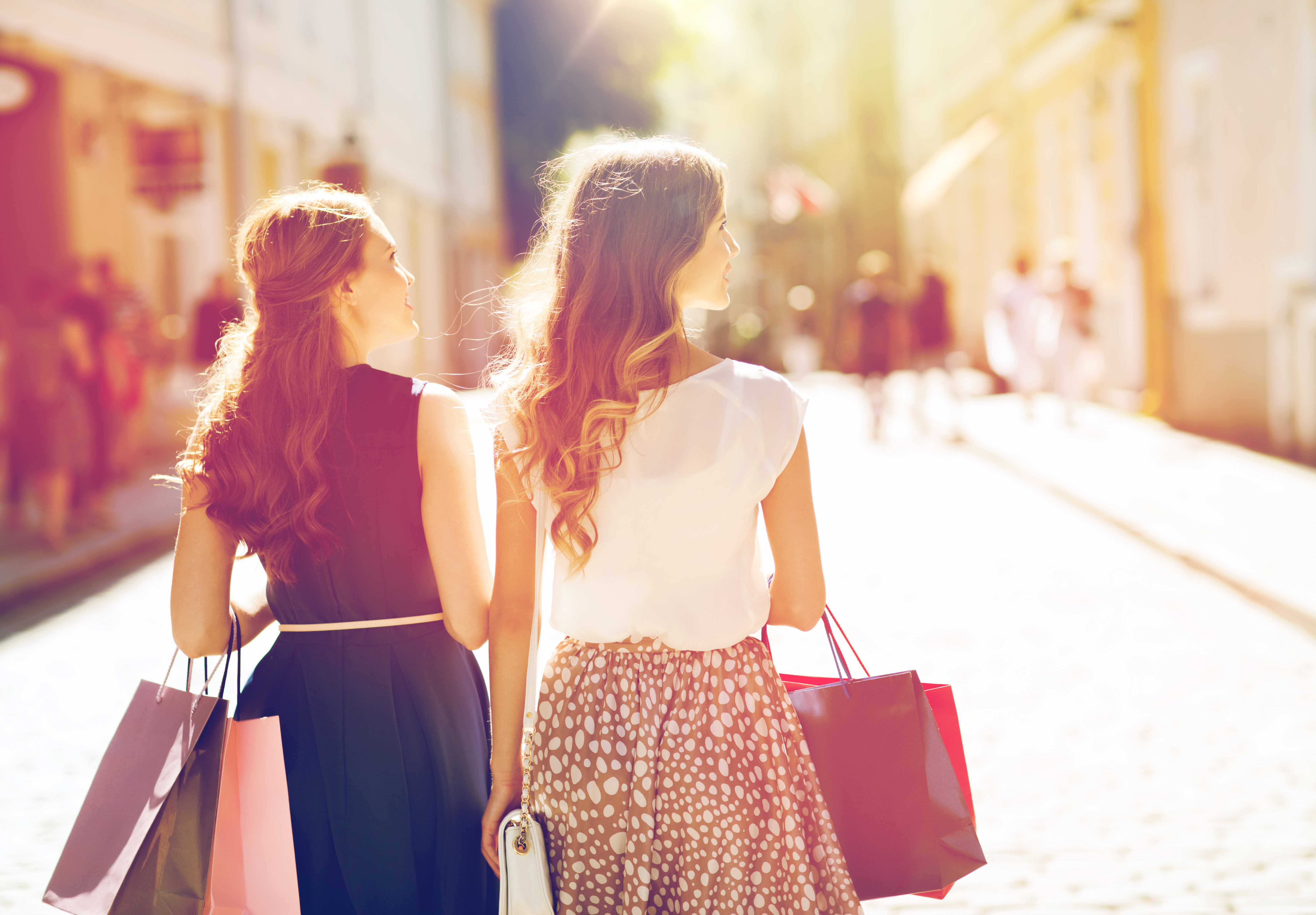 happy women with shopping bags walking in city